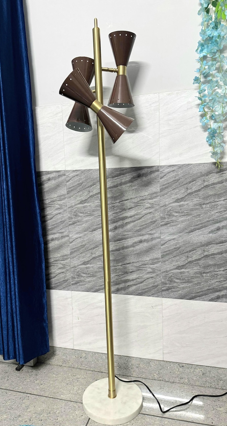 May include: A floor lamp featuring a tall, slender gold-toned metal pole mounted on a circular white base. The lamp has three brown, cone-shaped metal shades with small perforated holes along the edges, arranged at different heights and angles.