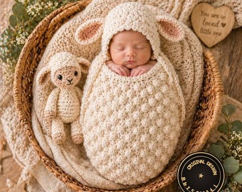 May include: A cream-coloured crochet baby cocoon with a matching lamb-ear hood, featuring a textured bobble stitch pattern. A small matching crochet lamb plush toy sits beside the swaddled infant inside a woven basket.