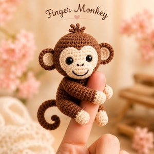 Puede incluir: Un mono de dedo de ganchillo en tonos marrón y crema, con una cara sonriente y grandes ojos negros. El texto "Finger Monkey" está encima del mono. El mono está posado en un dedo.