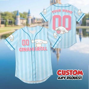 Op de afbeelding: Lichtblauw honkbalshirt met verticale strepen en de tekst "CINNAMAROLL" en het nummer "00" in roze. Het shirt heeft een stripfiguur en de woorden "YOUR NAME" op de achterkant. De tekst "CUSTOM ANY REQUEST" is ook zichtbaar.