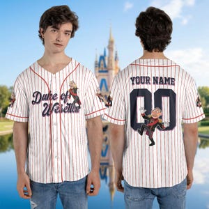 May include: White baseball jersey with red pinstripes, featuring the text "Duke of Weselton" and a cartoon character on the front. The back has "YOUR NAME" above a number and character graphic. Short-sleeved, button-down shirt.