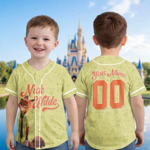 Puede incluir: Una camiseta de b&eacute;isbol verde claro con el personaje Nick Wilde de Zootopia. La camiseta tiene ribetes blancos, el nombre "Nick Wilde" en escritura naranja y el n&uacute;mero "00" en la espalda. La camiseta la lleva un ni&ntilde;o.