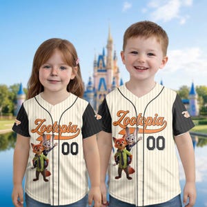 May include: Two children wearing cream-colored baseball jerseys with black sleeves. The jerseys feature the word "Zootopia" in orange script, the number "00", and a graphic of Nick Wilde and Judy Hopps.