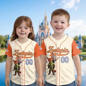 May include: Two cream-colored baseball jerseys with orange sleeves and trim. The jerseys feature the word "Zootopia" in orange script, the number "00" in blue, and cartoon characters. The background shows a castle.
