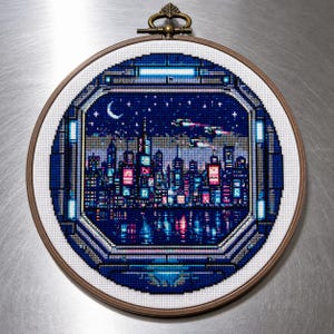 May include: A cross-stitch embroidery of a cityscape at night, framed in a wooden hoop. The scene features a dark blue sky with a crescent moon and stars, and a skyline of illuminated buildings reflected in the water below. The embroidery is in shades of blue, pink, and purple.