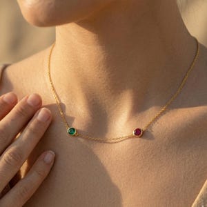 Op de afbeelding: Een fijne gouden ketting met een groene smaragd en een rode robijn. De edelstenen zijn in bezels gezet en verdeeld over de gouden ketting. De ketting wordt getoond op de hals van een persoon.