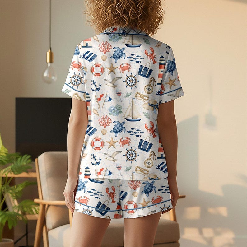 May include: Nautical-themed pajama set featuring a white background with blue, red, and orange illustrations of anchors, sailboats, sea turtles, and other marine elements. The short-sleeved top and shorts have blue trim.