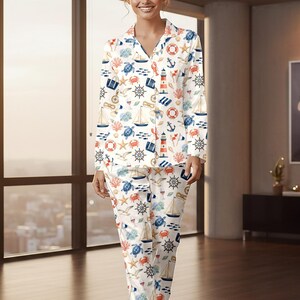 May include: White pajama set with a nautical theme. The long-sleeved top and pants feature a repeating pattern of sailboats, anchors, lighthouses, and sea creatures in blue, red, and orange. The pajamas have a collared neckline and button-down front.