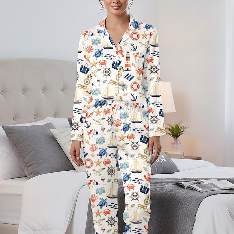 May include: White pajama set with a nautical theme. The long-sleeved top and pants are covered in a pattern of sailboats, anchors, sea turtles, and other marine elements in blue, red, and beige. The pajamas have a collared neckline and a relaxed fit.