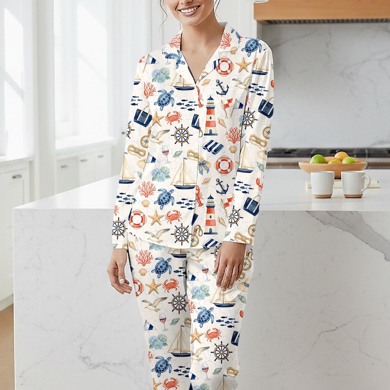 May include: White pajama set with a nautical pattern featuring sailboats, anchors, lighthouses, and sea creatures in blue, red, and beige. The long-sleeved top has a collared neckline and button closure. The matching pants complete the sleepwear set.