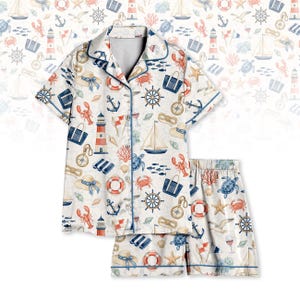 May include: White pajama set with a nautical pattern featuring anchors, sailboats, lighthouses, and sea creatures. The short-sleeved top and shorts have blue trim. The set is made of a soft, lightweight fabric.