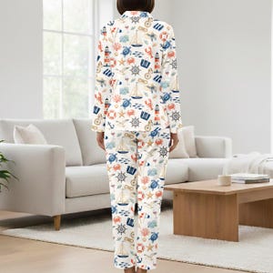 May include: White pajama set with a nautical theme. The long-sleeved top and pants are covered in a pattern of sailboats, anchors, lighthouses, crabs, and other sea-related images in blue, red, and beige.