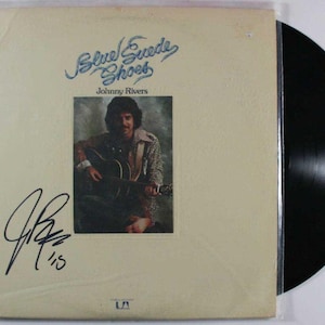 Puede incluir: Álbum de vinilo vintage titulado "Blue Suede Shoes" de Johnny Rivers. La portada del álbum presenta una foto del artista tocando la guitarra, con un autógrafo. El disco es negro y está en una funda de plástico.