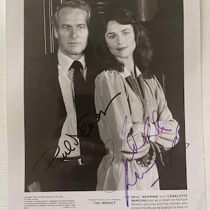 Könnte beinhalten: Schwarz-Weiß-Fotografie mit Paul Newman und Charlotte Rampling. Newman trägt Anzug und Krawatte, Rampling eine helle Bluse. Das Bild ist mit lila Tinte signiert. Der Text unten lautet "THE VERDICT".
