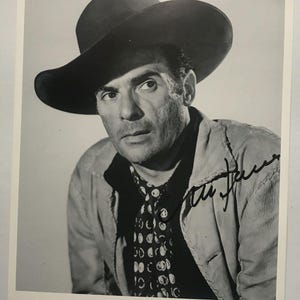 May include: A black and white photograph of a man in a cowboy hat and patterned scarf. The image is signed. The text at the bottom reads "THE OX-BOW INCIDENT". The man is looking directly at the camera.