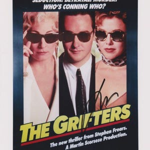 May include: Movie poster for "The Grifters" featuring John Cusack, Anjelica Huston, and Annette Bening. The poster has a dark background with the film's title in large, yellow letters. The tagline reads "Seduction. Betrayal. Murder. Who's conning who?"