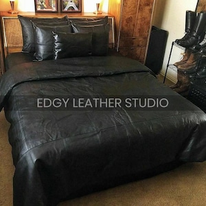 May include: A black leather bed set featuring a large duvet cover and five matching pillows. The surface of the bedding has a smooth, matte texture with visible stitched paneling. The text EDGY LEATHER STUDIO is centered on the image.