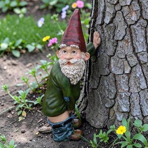 Può includere: Una statua di gnomo da giardino stravagante con un cappello a punta rosso, una giacca verde e pantaloni blu. Lo gnomo è appoggiato a un albero, con i pantaloni abbassati. La statua ha una lunga barba bianca ed è circondata da piante e fiori.