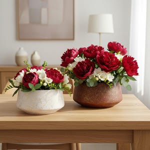 May include: Two floral arrangements with deep red peonies and white flowers. One is in a textured, off-white ceramic pot, the other in a brown, textured ceramic pot. Green foliage accents the flowers, creating a natural aesthetic.