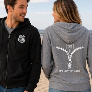 May include: Two zip-up hoodies, one black and one gray. The black hoodie has "Cape Cod Traffic Survivor" printed on the chest. The gray hoodie features a zipper graphic with the text "Merge Like a Zipper" and "It's Not That Hard."