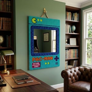 May include: A rectangular wall mirror featuring a tufted teal frame designed to resemble a vintage arcade game console. The frame includes a dark blue border, the text PAC-MAN, and a red box displaying SCORE HIGH SCORE 1980.