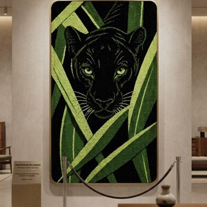 May include: A framed artwork titled "Panther in the Grass" depicts a black panther with piercing green eyes, partially obscured by stylized green foliage. The artwork is displayed in a gallery setting.