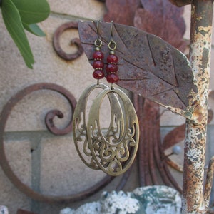 May include: Gold filigree earrings with red glass beads hanging from a rusty metal stand.