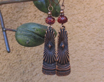 May include: A pair of copper earrings with a starburst design and red glass beads. The earrings are hanging from a branch.