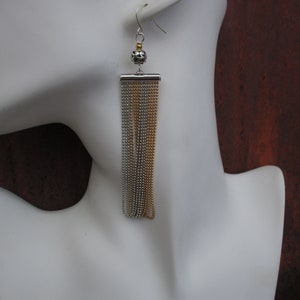 May include: Silver and gold chain earrings with a small black bead at the top.