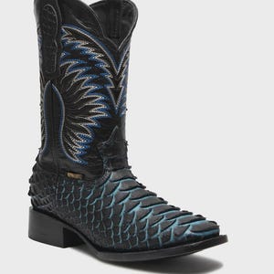 May include: A black western boot featuring a textured, scale-like pattern on the foot with blue highlights. The tall shaft displays intricate blue and white stitching in a flame-like design, complete with a square toe and a stacked block heel.