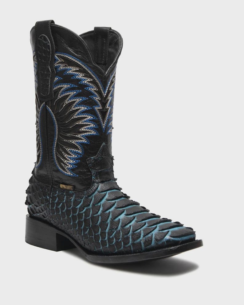 May include: A black western boot featuring a textured, scale-like pattern on the foot with blue highlights. The tall shaft displays intricate blue and white stitching in a flame-like design, complete with a square toe and a stacked block heel.