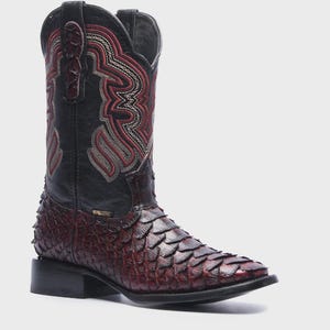May include: A mid-calf western boot featuring a dark red, textured scale-patterned vamp and a black leather shaft. The shaft is decorated with intricate red and white stitched embroidery patterns and includes black pull tabs at the top opening.