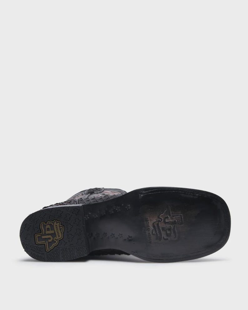 May include: A black leather western boot with a square toe and a stacked heel. The sole features a stamped logo with the letters JP inside a state of Texas outline, surrounded by a repeating star pattern and additional embossed branding.