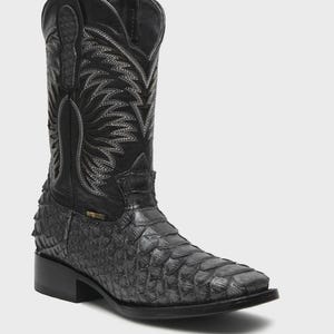 May include: A black western-style boot featuring a textured, scale-like pattern on the foot and a smooth leather shaft. The upper shaft is decorated with intricate grey stitching in a flame-like design, and the boot has a square toe profile.