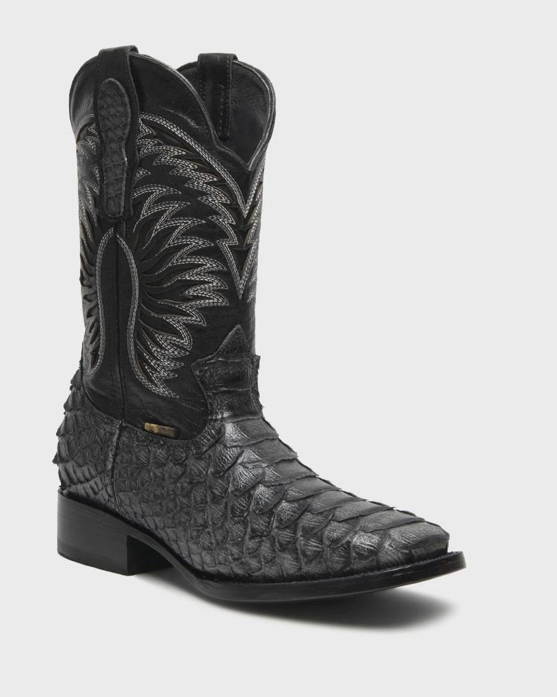 May include: A black western-style boot featuring a textured, scale-like pattern on the foot and a smooth leather shaft. The upper shaft is decorated with intricate grey stitching in a flame-like design, and the boot has a square toe profile.