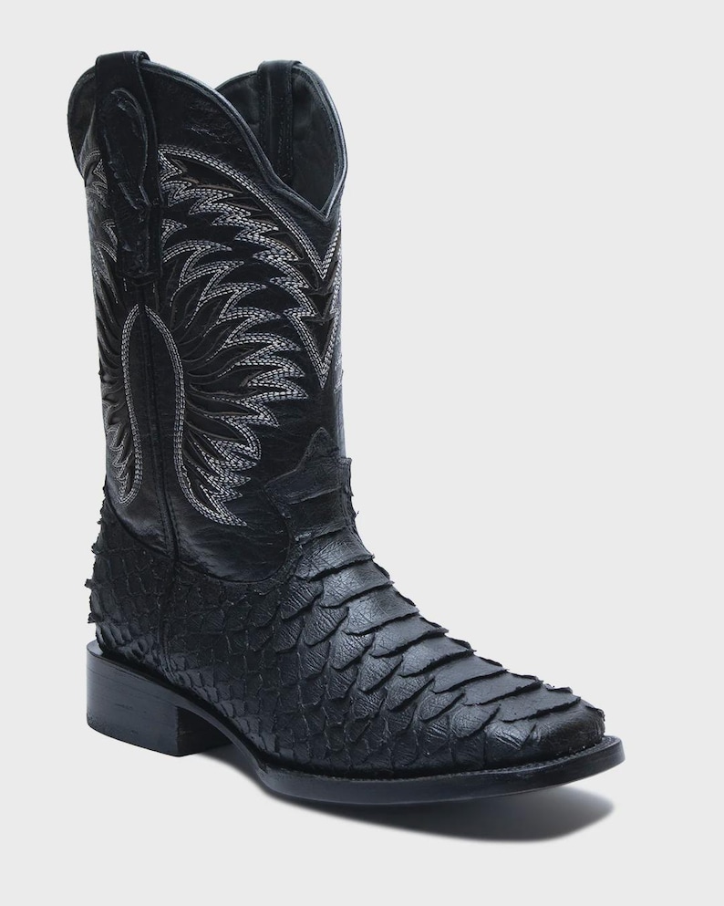May include: A black western-style boot featuring a textured, scale-like pattern on the foot and a smooth leather shaft. The upper shaft is decorated with intricate white stitching in a wing-like design, complete with pull tabs at the top.