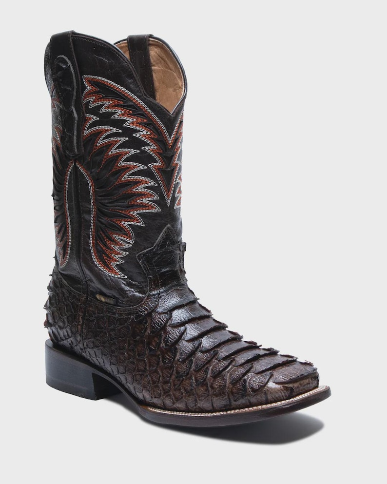 May include: A dark brown cowboy boot featuring a textured, scale-like leather vamp and a tall shaft with intricate red and white flame-patterned stitching. The boot has a square toe, a stacked heel, and pull tabs at the top of the shaft.