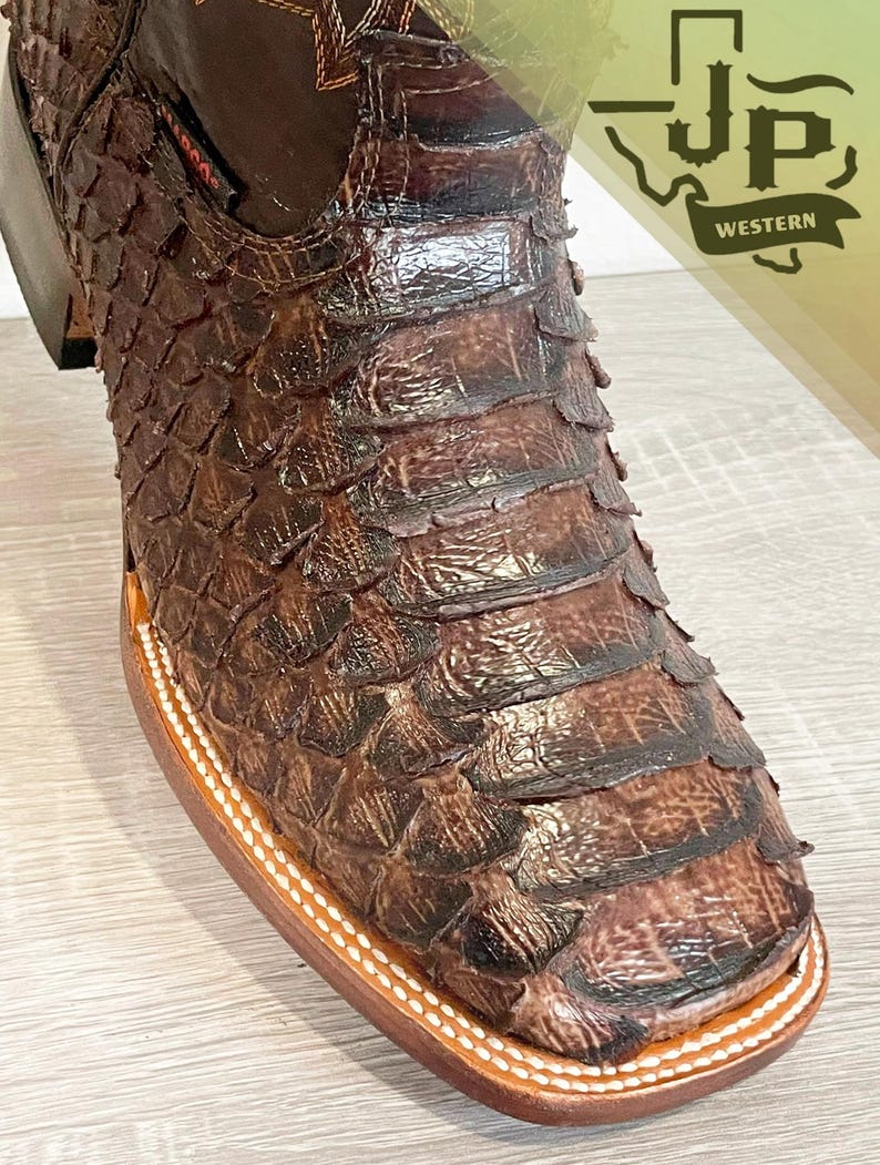 May include: A brown western boot featuring a textured, scale-like pattern across the vamp and toe. The boot has a square toe, a stacked heel, and white contrast stitching along the welt. A logo reading JP WESTERN is visible in the corner.