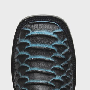 May include: A square-toe boot featuring a textured black leather surface with raised, scale-like patterns. The edges of the scales are highlighted with a vibrant blue finish, creating a distinct contrast against the dark black base material.