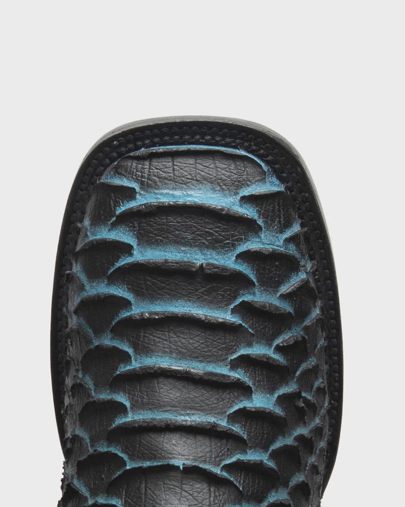 May include: A square-toe boot featuring a textured black leather surface with raised, scale-like patterns. The edges of the scales are highlighted with a vibrant blue finish, creating a distinct contrast against the dark black base material.