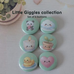 Op de afbeelding: Set van zes ronde knopen met schattige illustraties op een lichtgroene achtergrond. Ontwerpen omvatten een panda met een hart, een lachende wolk, een kaars, een potplant, een eend en een lachend hart. Tekst: "Little Giggles collection" en "Set of 6 buttons."