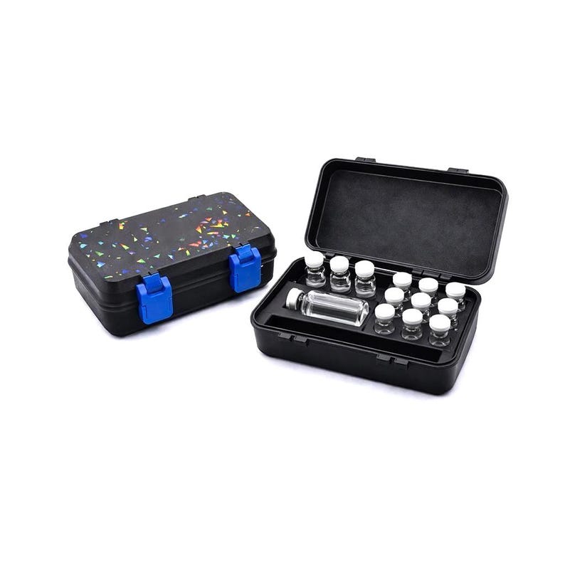 May include: Two black storage cases, one closed and one open, on a white background. The closed case has a speckled design with blue clasps. The open case reveals small glass vials and bottles, neatly arranged inside. The cases appear to be made of durable plastic.