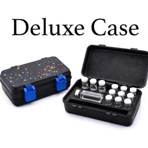 May include: Black Deluxe Case with blue clasps, closed and open, displaying small glass vials. The closed case has a speckled design. The open case reveals multiple vials with white caps. Text on top reads "Deluxe Case".