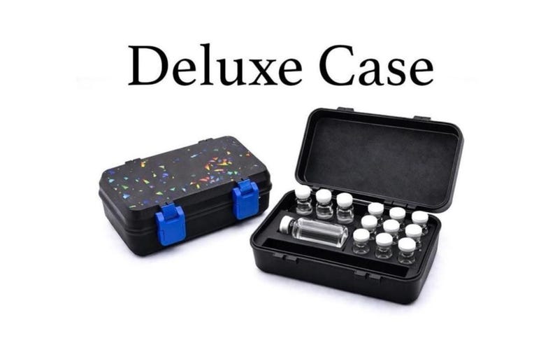 May include: Black Deluxe Case with blue clasps, closed and open, displaying small glass vials. The closed case has a speckled design. The open case reveals multiple vials with white caps. Text on top reads "Deluxe Case".
