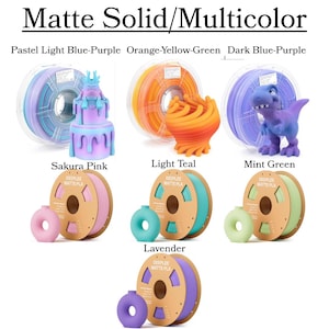 May include: A display of various 3D printing filaments in a range of colors, including pastel blue-purple, orange-yellow-green, and dark blue-purple. The image also shows 3D printed objects in matching colors, such as a cake and a dinosaur.