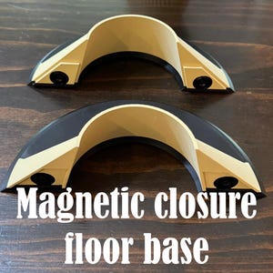 May include: Two semi-circular magnetic closure floor base components featuring a beige interior arch and a black outer frame. Each piece includes two small black circular magnets embedded on the front-facing angled sides. The text Magnetic closure floor base is printed in white at the bottom.