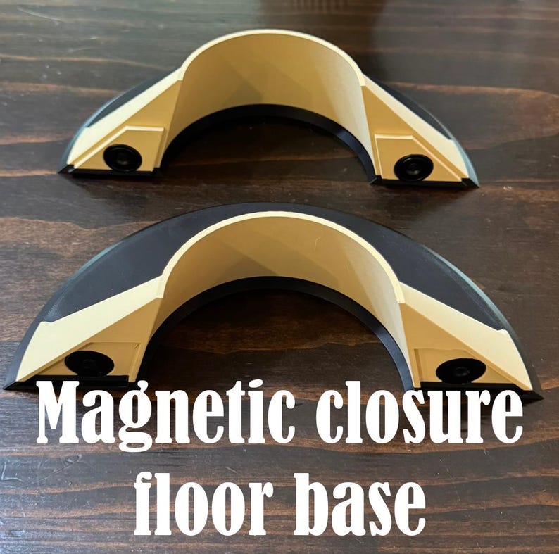 May include: Two semi-circular magnetic closure floor base components featuring a beige interior arch and a black outer frame. Each piece includes two small black circular magnets embedded on the front-facing angled sides. The text Magnetic closure floor base is printed in white at the bottom.