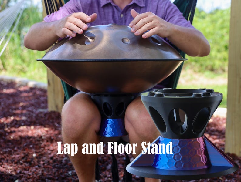 May include: A bronze-colored handpan instrument with circular tone fields, positioned above a black and blue hexagonal-patterned stand. The text Lap and Floor Stand is visible in white font. The stand features a wide base and open side cutouts.