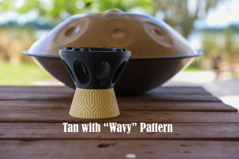 May include: A black and tan stand for a handpan instrument. The top section is black with circular cutouts, while the base is tan with a textured wavy geometric pattern. The text "Tan with "Wavy" Pattern" is printed below the stand.