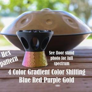 May include: A black handpan stand with a hexagonal pattern base featuring a 4 color gradient of blue, red, purple, and gold. Text on the image reads: Hex pattern, See floor stand photo for full spectrum, 4 Color Gradient Color Shifting Blue Red Purple Gold.